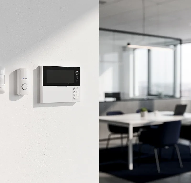 Alarmcentrale op kantoorwand met bewegingssensoren, glazen scheidingswanden en neutraal interieur op de achtergrond.